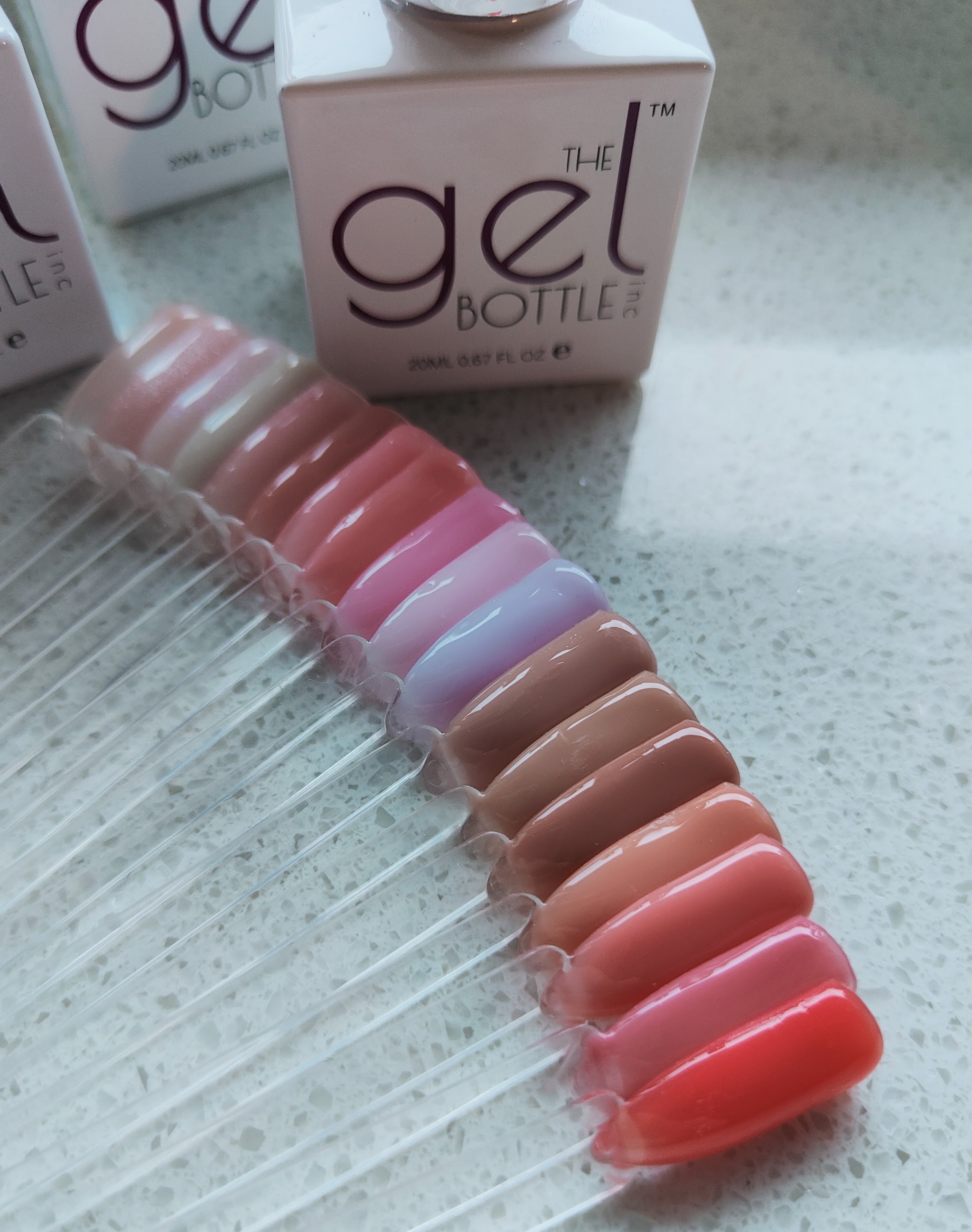 Een waaier met kleurstalen in nude, roze en rood naast flesjes van The GelBottle