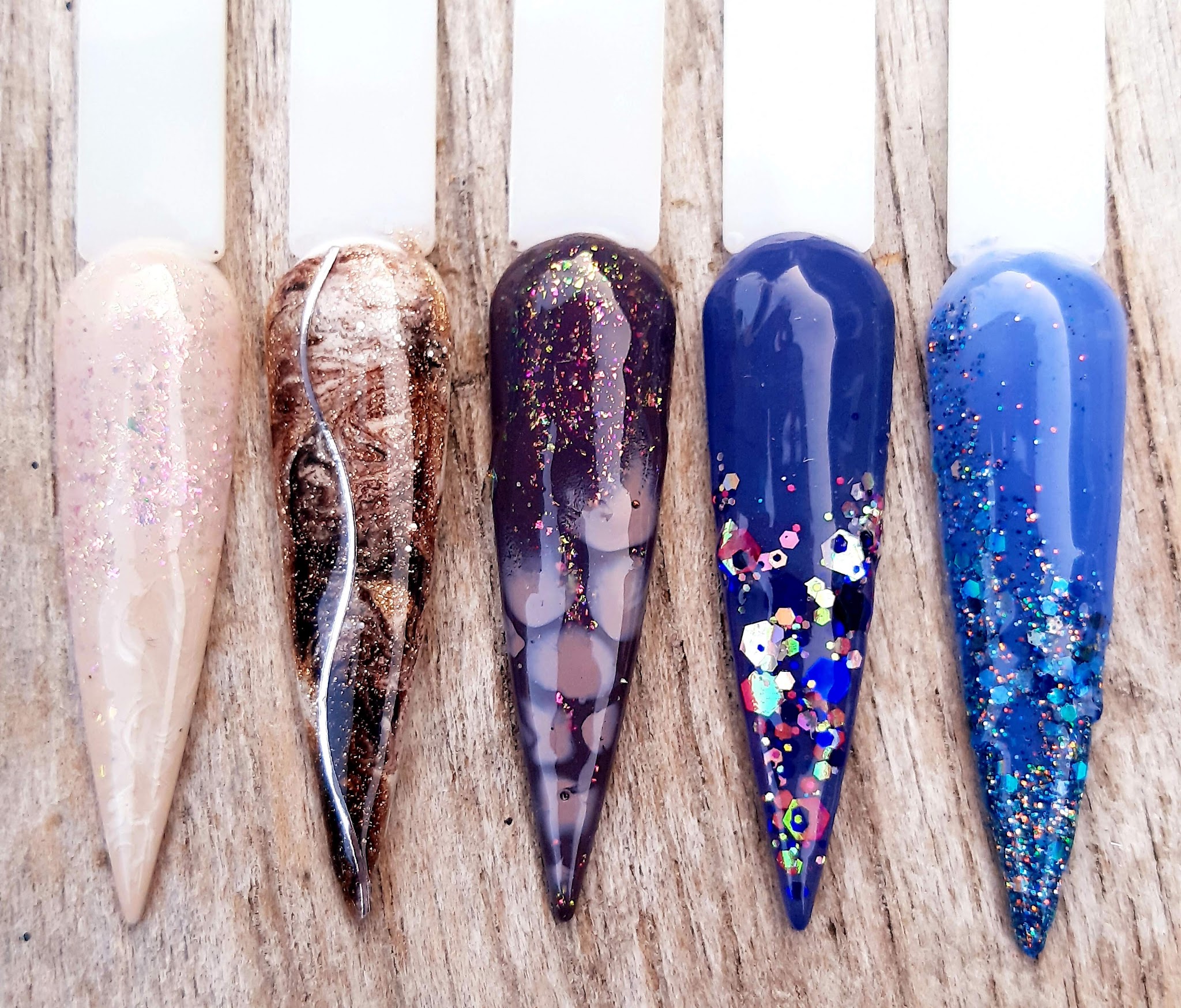 Vijf lange voorbeeldtips met marmer, glitter en blauwe nail art op een houten standaard